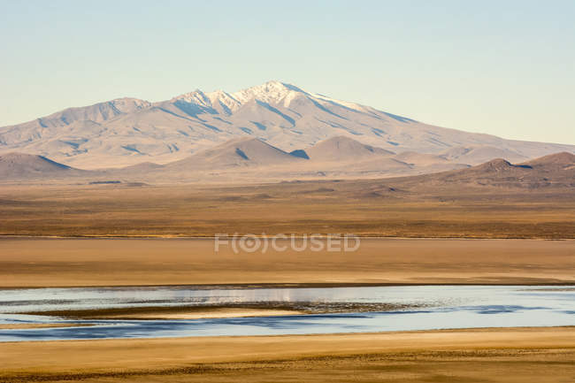 Un atardecer pone de manifiesto los colores de una laguna en un desierto sudamericano con un pico nevado en el horizonte, Malargue, Mendoza, Argentina - foto de stock