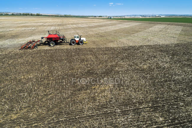 Trator puxando um semeador de ar, semeando um campo com céu azul na distância — Fotografia de Stock