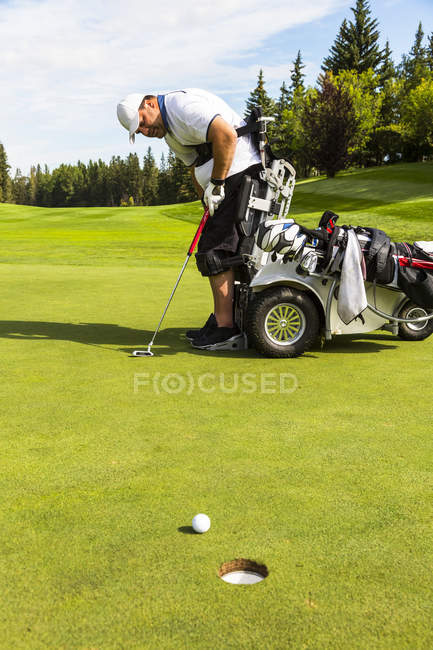 Un golfeur physiquement handicapé mettant une balle sur un terrain de golf et utilisant un fauteuil roulant hydraulique motorisé d'assistance au golf, Edmonton, Alberta, Canada — Photo de stock