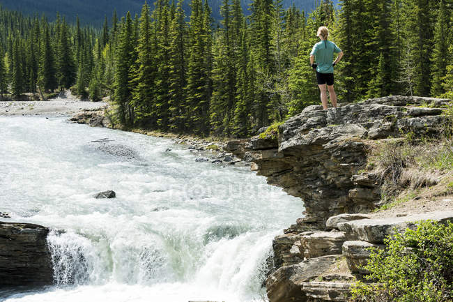 Female hiker standing on top of rock cliff overlooking waterfalls and rushing river,  Alberta, Canada — Stock Photo