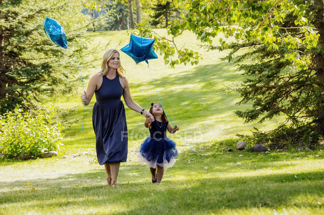 Mother walking through a park with daughter and holding balloons — Stock Photo
