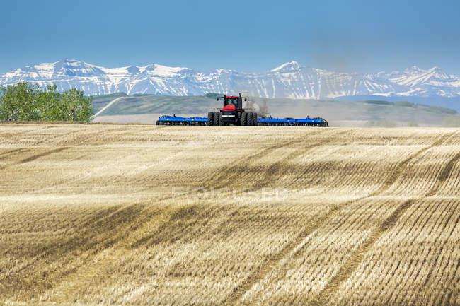 Traktor zieht eine Sämaschine, sät ein Feld mit Bergen und blauem Himmel im Hintergrund — Stockfoto
