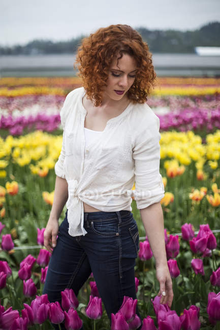 Beautiful red hair woman standing in field of tulips — Stock Photo