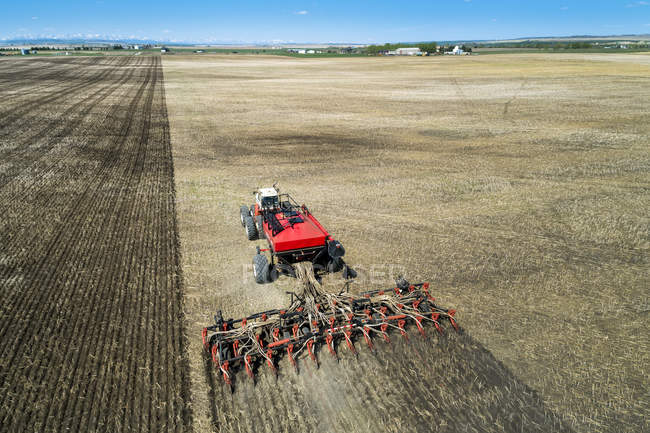Трактор тягне повітряну седу, посіявши поле з блакитним небом на відстані — стокове фото