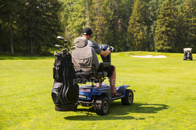 Um golfista fisicamente deficiente dirigindo uma cadeira de rodas de golfe especializada entre buracos em um campo de golfe durante um torneio, Edmonton, Alberta, Canadá — Fotografia de Stock