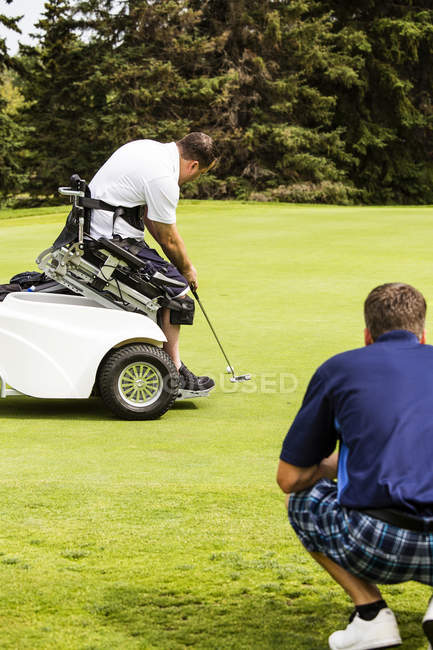 Un golfista discapacitado físicamente usando una silla de ruedas especializada que se desliza y conduce una pelota por el fairway de un campo de golf, Edmonton, Alberta, Canadá - foto de stock