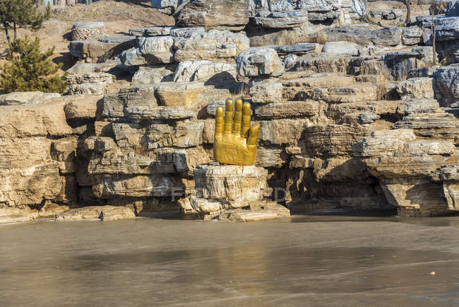 Буда протягивает руку вдоль замерзшего озера Янг Гротт, древнекитайского буддистского искушения гроттов недалеко от Фунга; Китай — стоковое фото