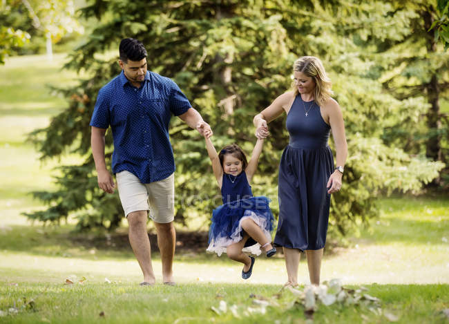 Mother and father in mixed race marriage walking and swinging their little girl in park — Stock Photo