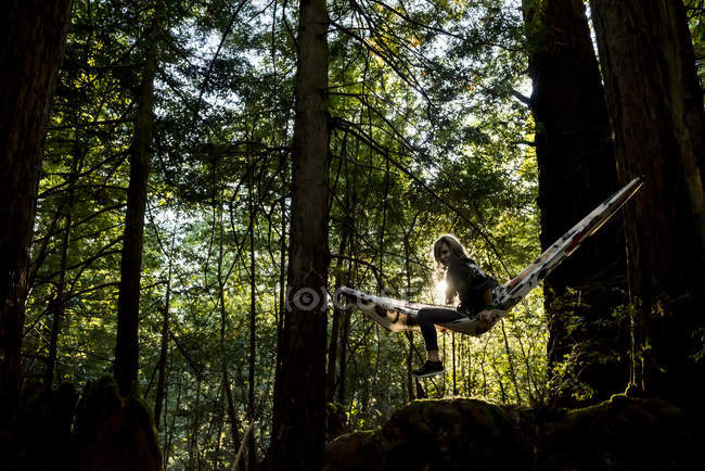 Mulher sentada em uma rede em uma floresta ao pôr do sol — Fotografia de Stock
