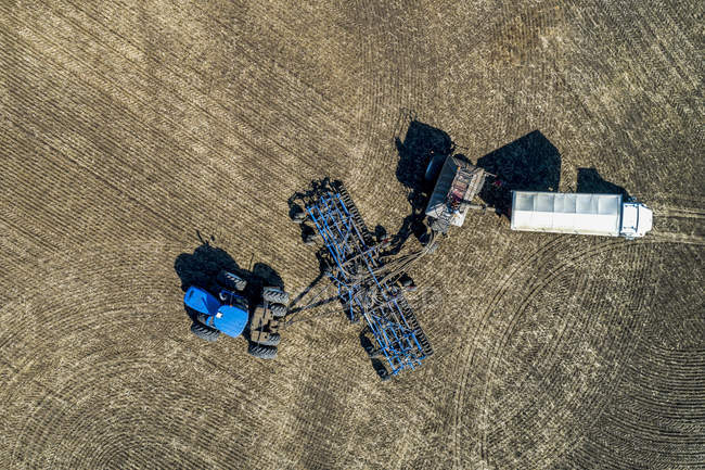 Vista aérea do agricultor enchendo um funil de semeadora de ar com um caminhão em um campo com céu azul no fundo — Fotografia de Stock