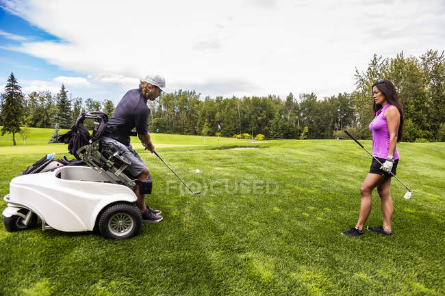 Um golfista fisicamente deficiente usando uma cadeira de rodas especializada teeing off e dirigindo uma bola no fairway de um campo de golfe, Edmonton, Alberta, Canadá — Fotografia de Stock