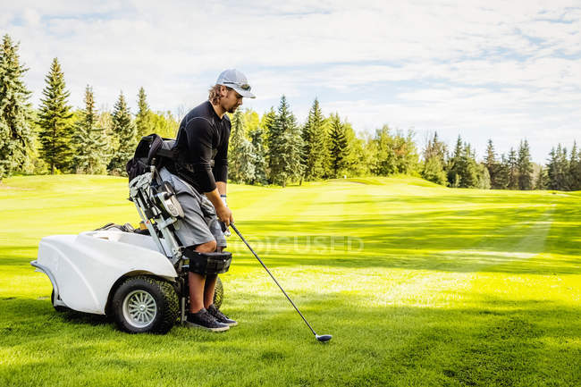 Un golfeur physiquement handicapé utilisant un fauteuil roulant spécialisé aligne son conducteur avec la balle sur le terrain de golf, Edmonton, Alberta, Canada — Photo de stock