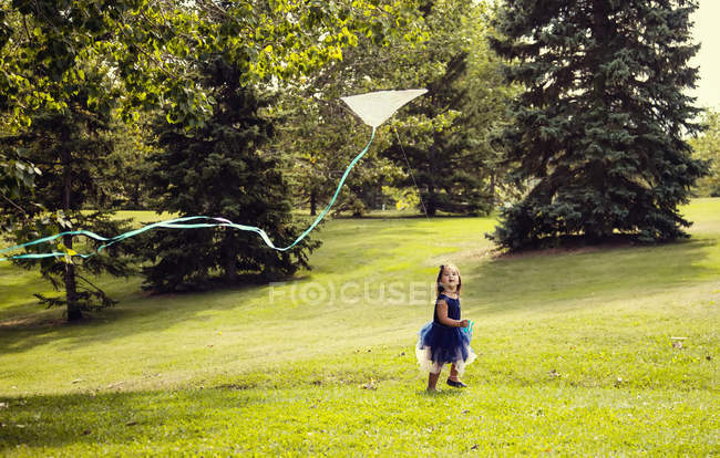 Uma jovem garota em um vestido correndo e voando um papagaio no parque — Fotografia de Stock