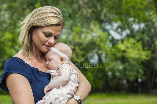 Young mother cuddling her sleeping baby outdoors in a park — Stock Photo