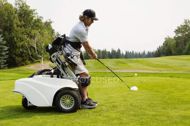 A physically disabled golfer driving a ball on a golf green and using a specialized golf assistance motorized hydraulic wheelchair, Edmonton, Alberta, Canada — Stock Photo