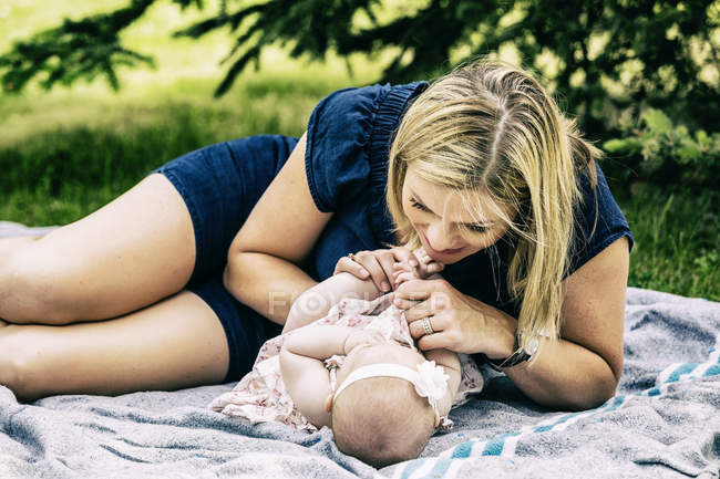 Jovem mãe brincando com seu bebê em um cobertor em um parque da cidade — Fotografia de Stock