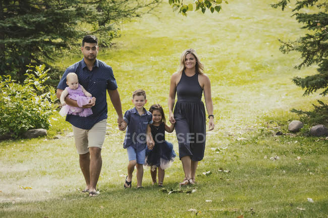 A mother and father in a mixed race marriage walking with their kids in a park on a family outing during a warm fall day — Stock Photo