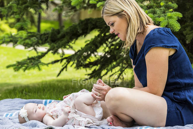 Joven madre jugando con su bebé en una manta en un parque de la ciudad - foto de stock