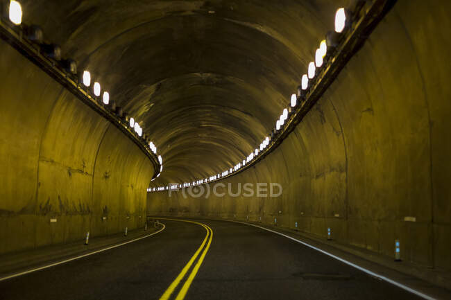 Road leading through a concrete tunnel with lights in the Fraser Canyon; British Columbia, Canada — Stock Photo