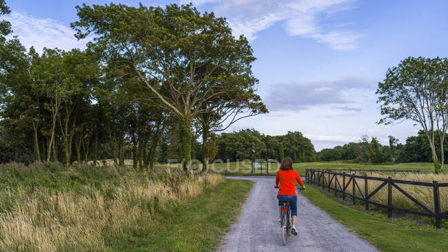 Mujer montando su bicicleta por un camino en Gleno Abbey Hotel and Golf Course; Condado de Galway, Irlanda - foto de stock