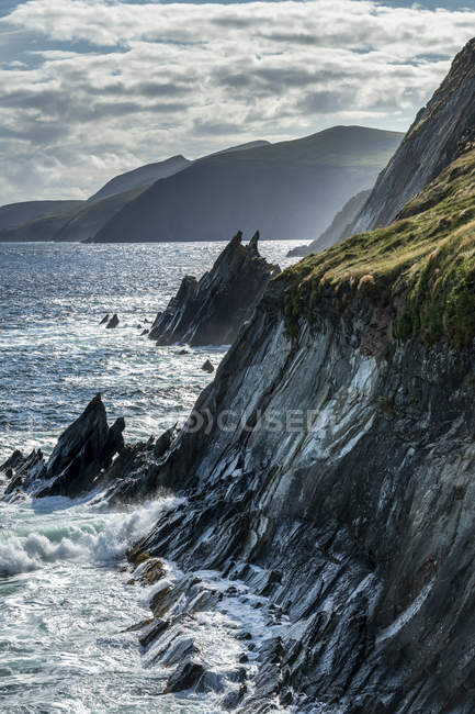 Vista panorámica de la escarpada costa del Condado de Kerry con el agua salpicando en los acantilados rocosos, Ballyferriter, Condado de Kerry, Irlanda - foto de stock