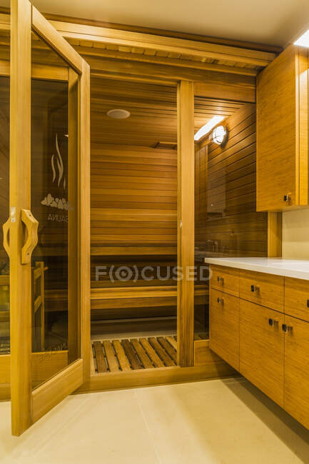 Sala de sauna en el baño del sótano con tocador de madera de bambú y suelo de mármol blanco en el interior de cedro manchado de lujo y casa de madera; Quebec, Canadá - foto de stock
