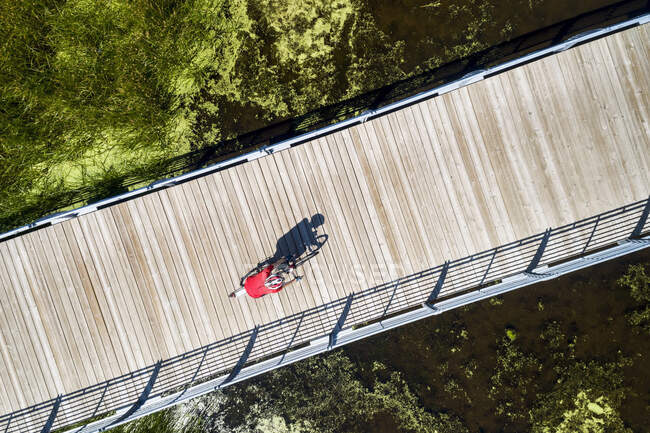 Aerial view looking straight down on a female cyclist on a bridge across a swampy pond with shadow of cyclist, East of Calgary; Alberta, Canada — Stock Photo