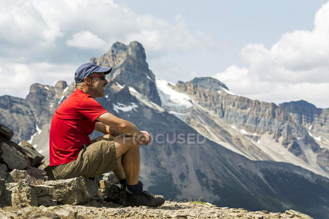 Senderista masculino sentado en una zona rocosa con vistas a la montaña en el fondo; Columbia Británica, Canadá - foto de stock