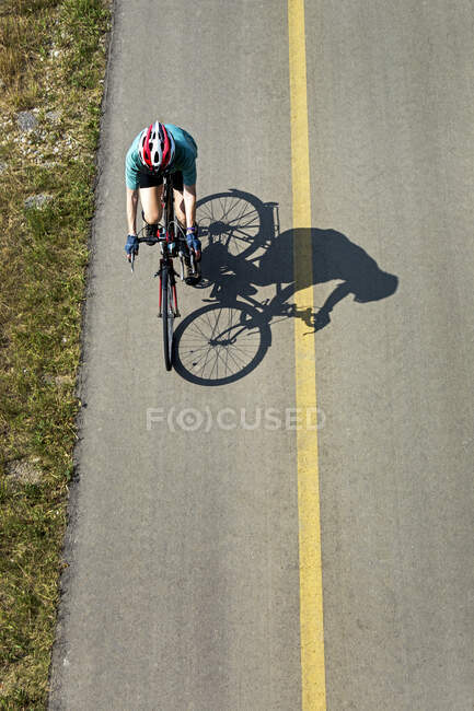 Aerial view looking down on a female cyclist on a paved pathway with shadow of cyclist; Calgary, Alberta, Canada — Stock Photo