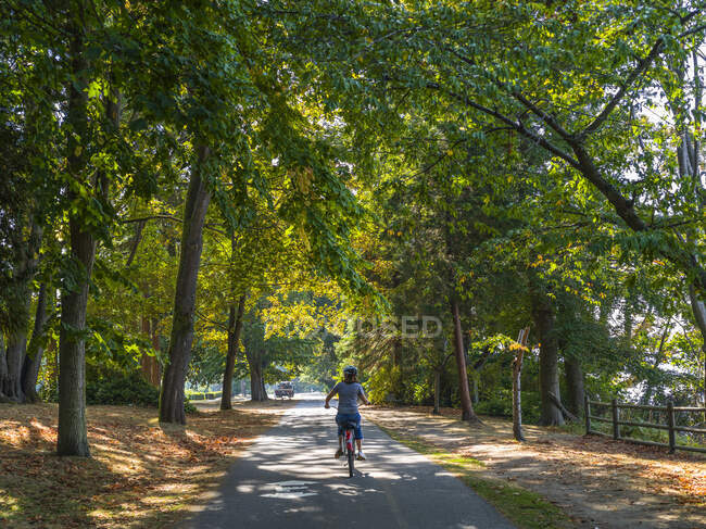 Woman riding a bike along Stanley Park Seawall trail; Vancouver, British Columbia, Canada — Stock Photo