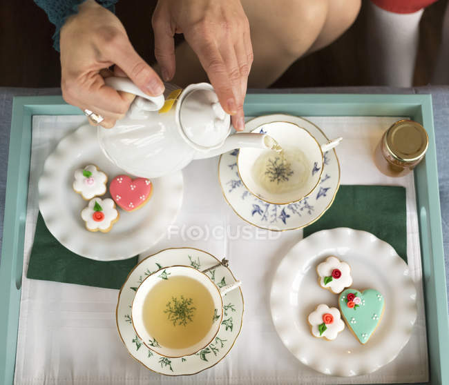 Woman pouring tea into teacups with saucers and served with fancy cookies; Surrey, British Columbia, Canada — Stock Photo