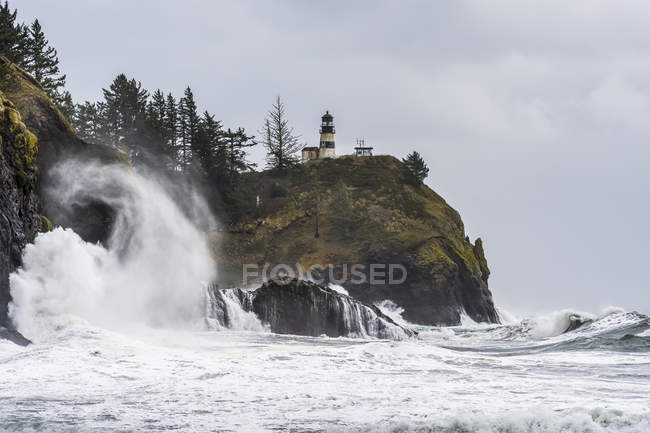 Surf fills the air with salt spray at Cape Disappointment with a lighthouse up on the ridge; Ilwaco, Washington, United States of America — Stock Photo
