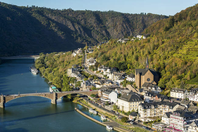 High view of riverside village with stone church and steep hillside slopes with stone bridge crossing; Cochem, Germany — Stock Photo