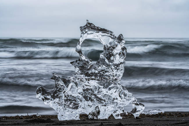 Piece of ice on Diamond Beach, near Jokusarlon, with the ocean behind it along the South coast of Iceland; Iceland — Stock Photo