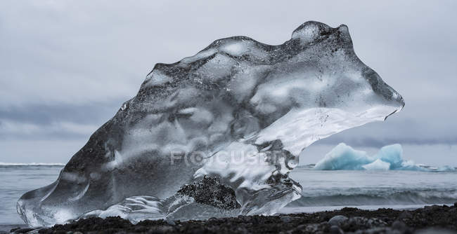 Кусок льда на Даймонд-Бич, недалеко от Джокосарлона, с океаном позади него вдоль южного побережья Исландии; Исландия — стоковое фото