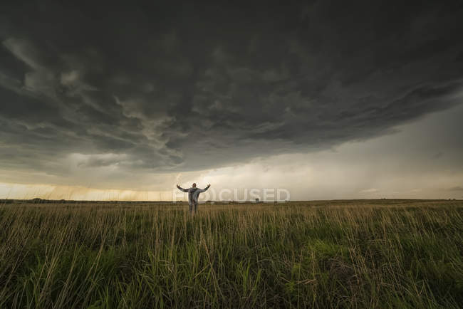 Homem em pé no campo observando a tempestade se aproximando; Kansas, Estados Unidos da América — Fotografia de Stock