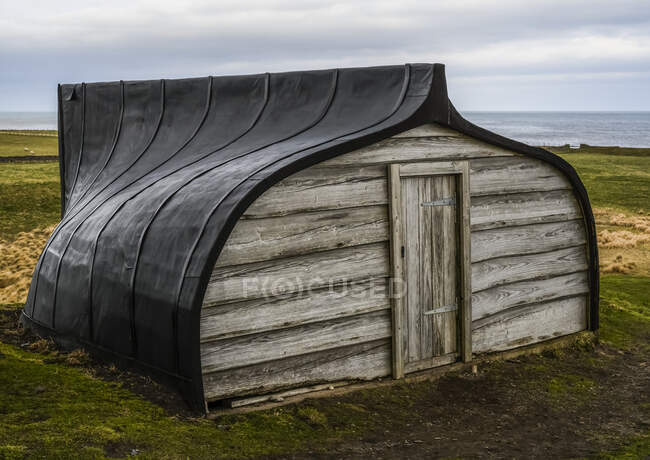 Barco de pesca revertido utilizado como cobertizo; Isla Santa, Northumberland, Inglaterra - foto de stock
