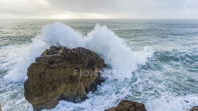 Grande onda che si schianta contro una roccia lungo una costa. Le onde più grandi del mondo sono qui a Nazare; Nazare, Distretto di Leiria, Portogallo — Foto stock