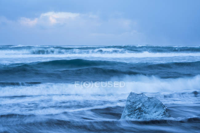 Großer Eisblock, der an der Küste von Südisland liegt, während Wellen auf die Küste krachen; Island — Stockfoto