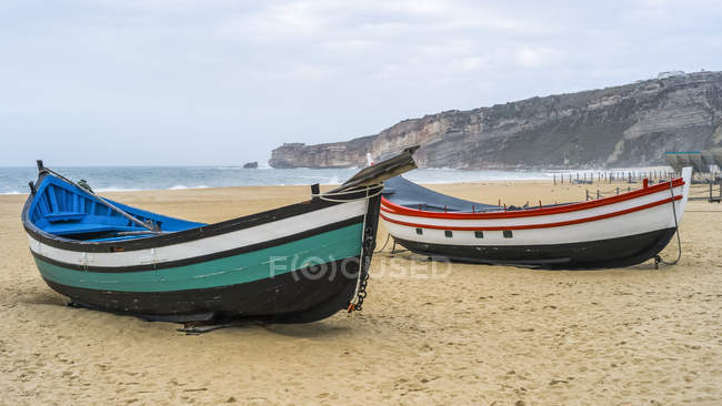 Dos coloridos botes de remos de madera en la playa en la ciudad balnearia de Nazare; Nazare, Leiria District, Portugal - foto de stock