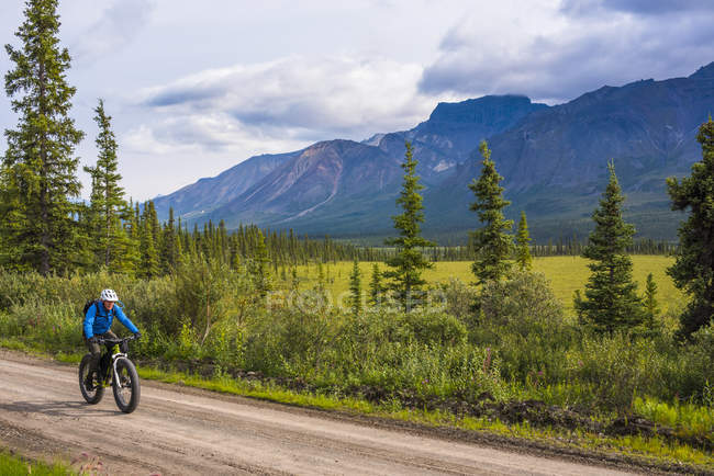 Man fat biking on the Nabesna Road in Wrangell - St. Elias National Park and Preserve on a cloudy summer day in South-central Alaska, United States of America — стокове фото