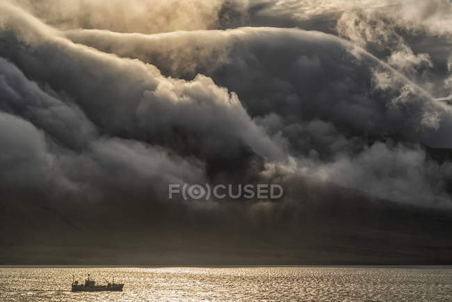 Nave da pesca con nuvole drammatiche che scorrono sulle montagne; fiordi orientali, Islanda — Foto stock