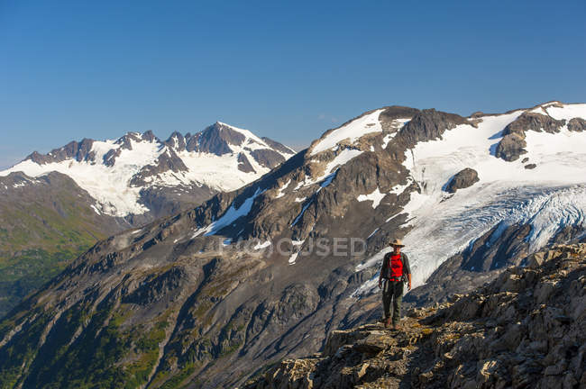 Homme marchant près du sentier du champ de glace Harding avec les montagnes Kenai et un glacier suspendu sans nom en arrière-plan, parc national des Fjords de Kenai, péninsule de Kenai, centre-sud de l'Alaska, États-Unis d'Amérique — Photo de stock