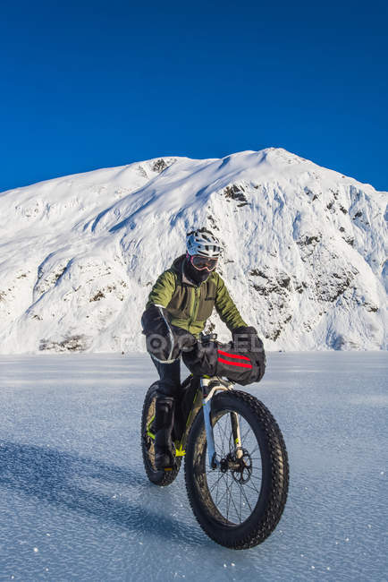 Man riding fatbike across frozen Portage Lake in mid-winter in South-central Alaska, Estados Unidos da América — Fotografia de Stock