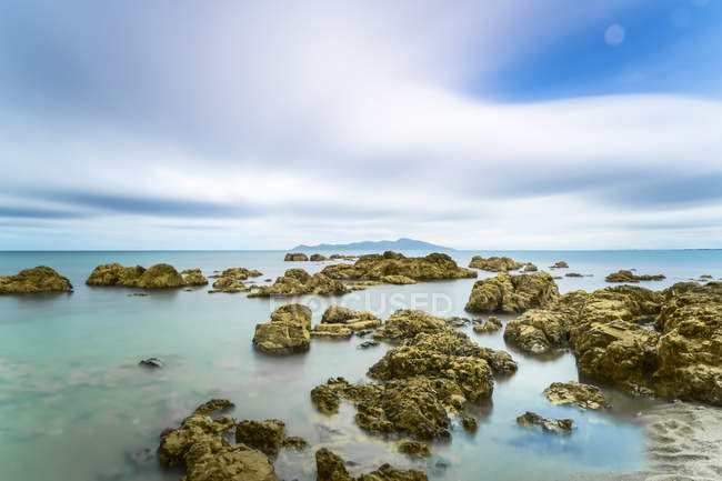 Rocas en el océano a lo largo de la costa en Pukerua Bay, Kapiti Island; Wellington, Nueva Zelanda - foto de stock