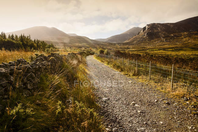 A gravel trail leads through a mountainous landscape at sunrise, Brandy Pad, Mourne Wall, Spellack, County Down, Ireland — Stock Photo
