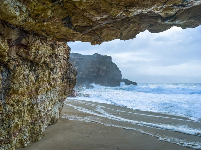 Praia de Nazare com falésias acidentadas e ondas ásperas; Nazare, Distrito de Leiria, Portugal — Fotografia de Stock