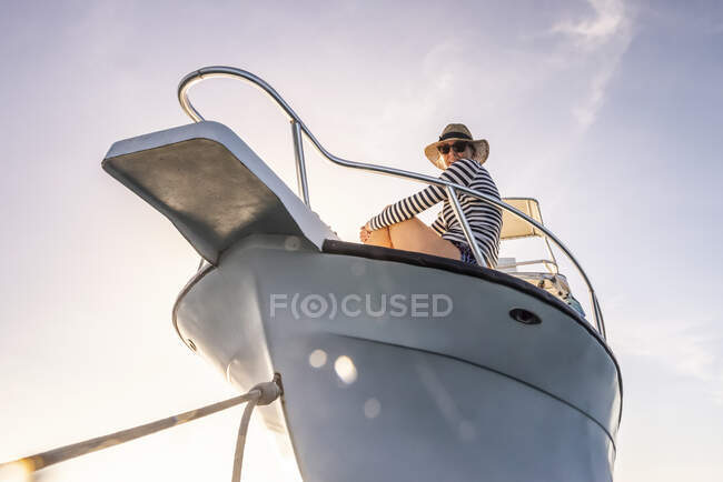 Woman wearing sunglasses and a sun hat looking down at the camera from the deck of a boat against a blue sky with sunlight; Bay Islands Department, Honduras — Stock Photo