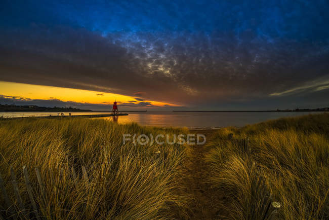 Herd Groyne Lighthouse and dramatic sunset with glowing clouds and tide washing onto beach in the foreground, South Shields, Tyne and Wear, England — Stock Photo