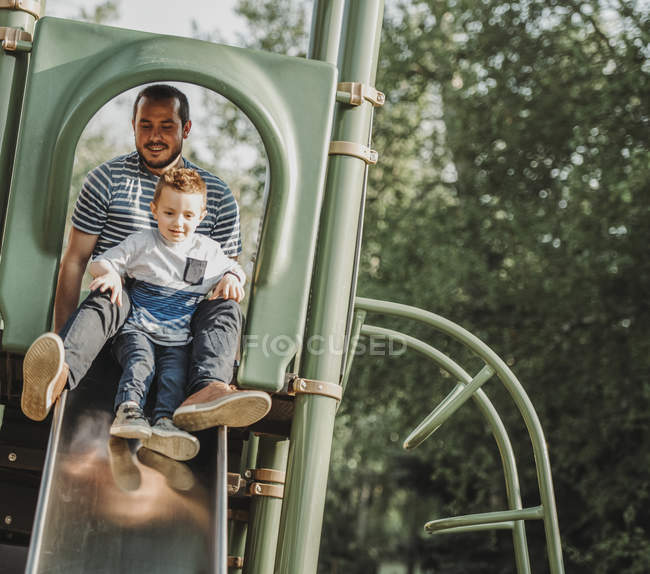 Pai em um slide com o filho jovem; Edmonton, Alberta, Canadá — Fotografia de Stock